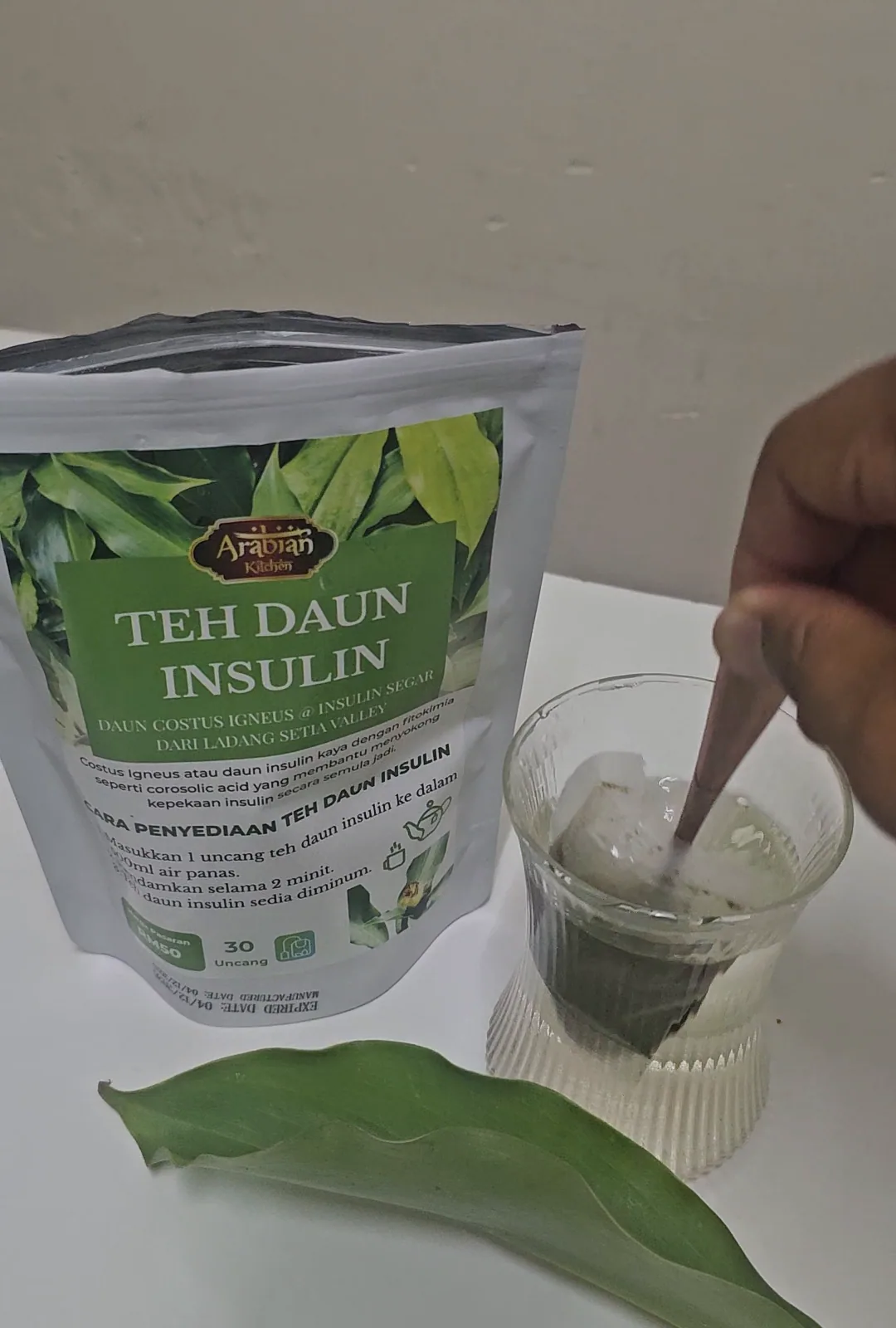 Sesudu daun kering yang dikisar halus di sebelah pek Teh Daun Insulin